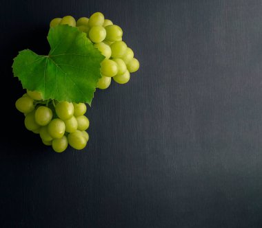 Bir demet üzüm. Tarım ve şarap üretimi kavramı. Koyu kırsal arka planda yaprakları olan üzüm demetleri. Düz şarap kompozisyonu siyah masanın üzerinde yatıyordu. Web pankartı