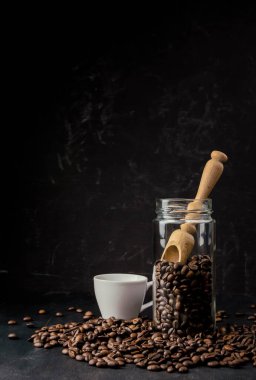 Cam kavanozdaki kahve çekirdekleri. Kavrulmuş fasulye. Siyah Americano kahvesi. Kahve çekirdekli kahve fincanı. Kahve dükkanı konsepti, kahve severler ve uzmanlar. Karanlık bir arka planda kavanoz. Günaydın..