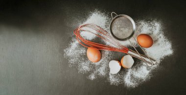 Pişirme arka planı. Pişirme, pişirme arka planı için gerekli malzemeler. Siyah zemin üzerinde un, şeker, yumurta ve çatal bıçak. Kopyalama alanı olan üst görünüm.