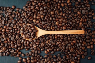 Kahve çekirdekleri ve tahta kaşık. Koyu kahve çekirdekleri. Kavram: kahve çekirdekleri ihraç ve ithalatı, kahve tüketimi. Reklam için fotokopi alanı olan taze kavrulmuş kahve taneleri.