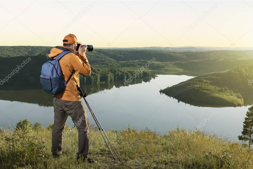 Mature traveller man with backpack standing in mountain and taking a photo. Happy man hiking with backpack at sunset.