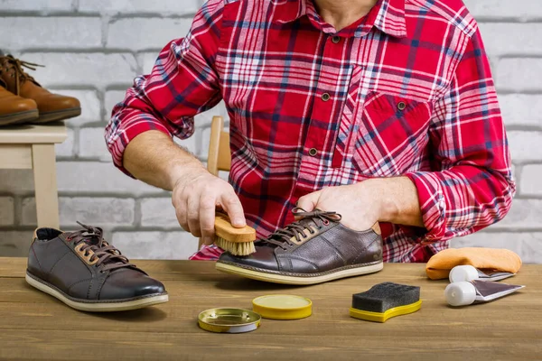 Man polishing leather shoes with brush on wooden table of workplace. Small business.