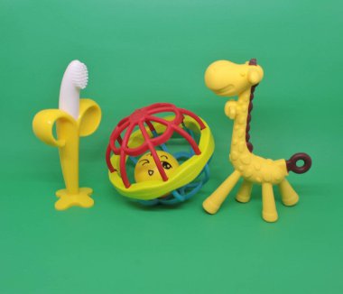 Renkli bebek çıngırakları ya da bağcıkları yeşil arka planda izole edilmiş, bebek dişlerinin büyümesini teşvik etmek için..