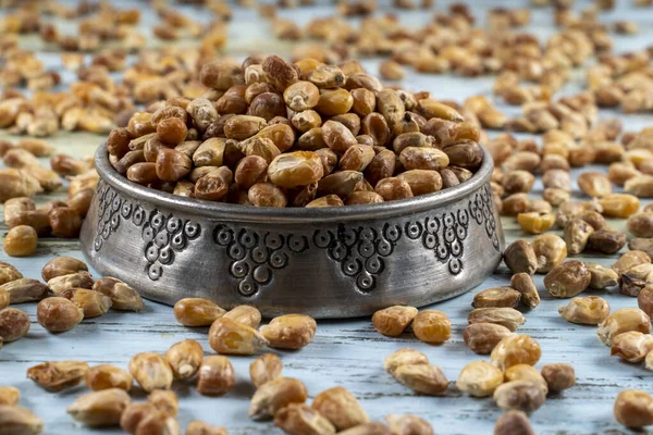 Roasted corn nuts in a metal bowl and roasted corns scattered around