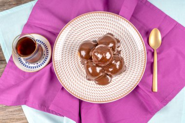 Lezzetli profiteroller ve bir bardak çayla servis edilen bir tabakta çikolata..
