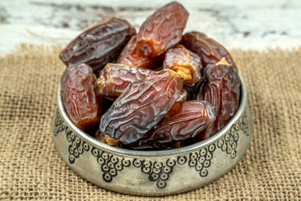 close up picture of dates palm fruit in a silver bowl on wooden table background. Dates palm fruit dry is snack healthy.