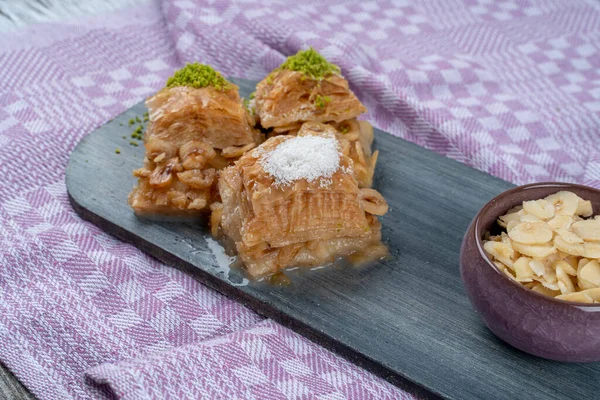 Tahta tepside fındıklı fındıklı fındıklı sütlü baklava, Türk baklavası, yerel adı Sutlu nuriye baklava veya sütlü baklava ile servis edilir.