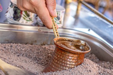 Sıcak kumda geleneksel Türk kahvesi hazırlandı. Sıcak altın kumda Türk kahvesi yapmak için seçici bir odak. Kahve hazırlama konsepti. Alternatif ve eski kahve demleme metodu.