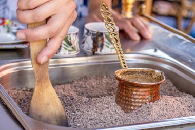 Sıcak kumda geleneksel Türk kahvesi hazırlandı. Sıcak altın kumda Türk kahvesi yapmak için seçici bir odak. Kahve hazırlama konsepti. Alternatif ve eski kahve demleme metodu.