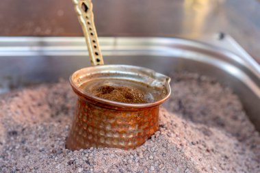 Sıcak kumda geleneksel Türk kahvesi hazırlandı. Sıcak altın kumda Türk kahvesi yapmak için seçici bir odak. Kahve hazırlama konsepti. Alternatif ve eski kahve demleme metodu.