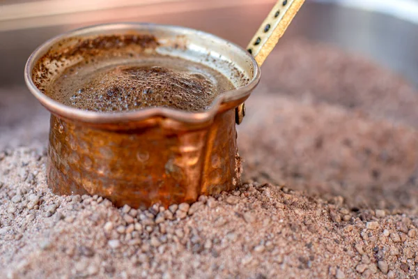 Traditional turkish coffee in cezve prepared on hot sand. Selective focus making turkish coffee on hot golden sand. Coffee preparation concept. Alternative and old method of brewing coffee.