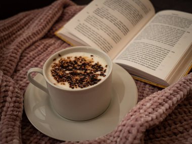 Yumuşak odaklanma, sonbaharda evde yaşam tarzı, kızlık zarı stili, arka planda açık kitap yumuşak bir kazak, kakaolu süt, dinlenme zamanı. 