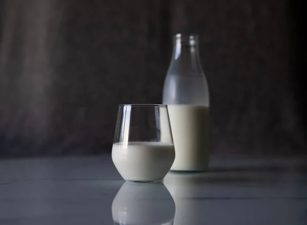 Glass with white milk on the table. Against the background, not a full bottle of milk is out of focus. High quality photo