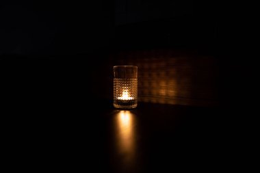 Bardakta mum. Işık ışınları camın duvarlarından kırılarak geçer. Masaya mum ışığı yansıması ve yüksek kaliteli fotoğraf.