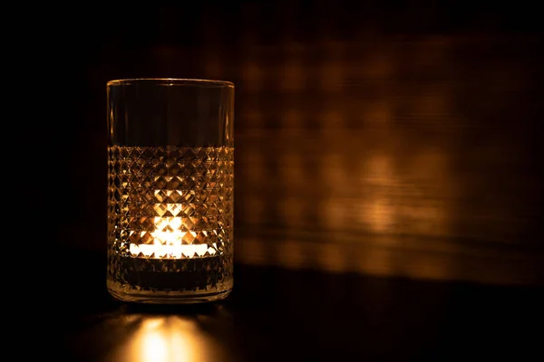 Candle in a glass. Rays of light are refracted through the walls of the glass. Reflection of candle light on the table and wall. High quality photo
