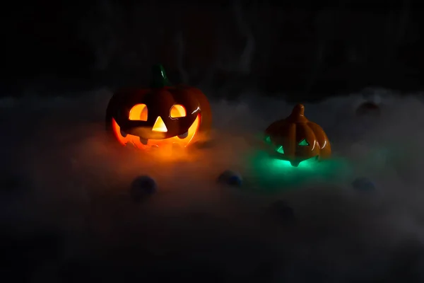 Halloween pumpkin face lantern at night with misty smoke. Two pumpkins glow with bright colors.Thick gray smoke comes out and spreads across the black table. High quality photo