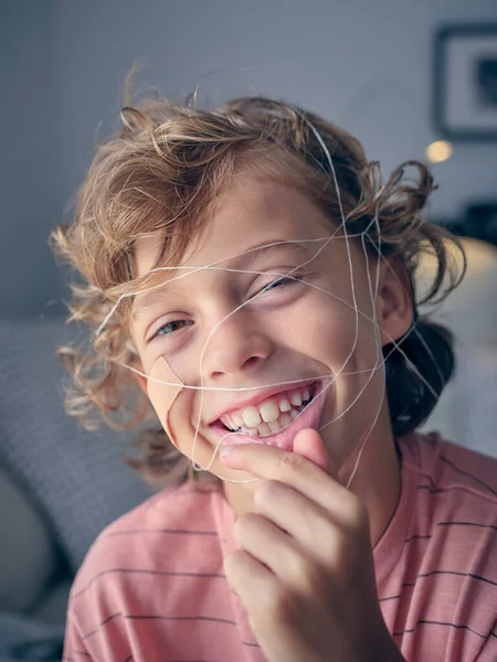 Positive boy with thread on face looking at camera with smile while preparing for pulling out tooth in light living room