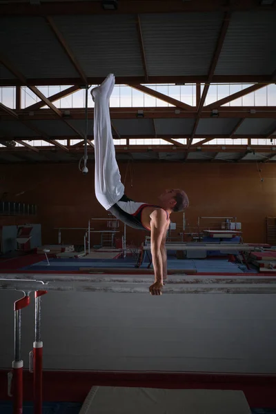 Young male gymnast doing exercises on the parallel apparatus.
