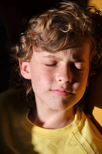 Mindful child with freckled face skin and brown hair in yellow wear resting in sunlight