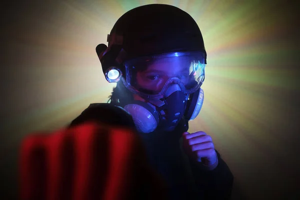 Aggressive child in protective gas respirator looking at camera with clenched fists during heist in dark mint with glowing neon lights