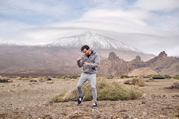 Full body of young male in sportswear standing on grassy stony ground and boxing while resting in highlands near volcanic area of Teide mountain in Tenerife in Canary Islands