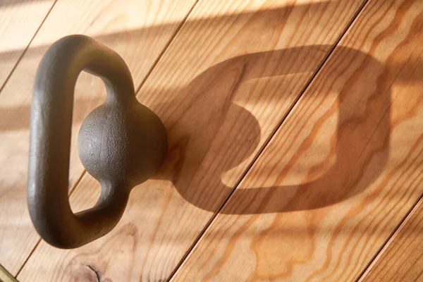 High angle of heavy metal kettlebell with large handle placed on wooden floor in daylight