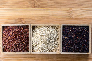 Ahşap arka planda kırmızı, siyah ve beyaz kinoa tohumları. Vejetaryen yemeği.