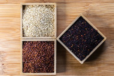 Ahşap arka planda kırmızı, siyah ve beyaz kinoa tohumları. Vejetaryen yemeği.