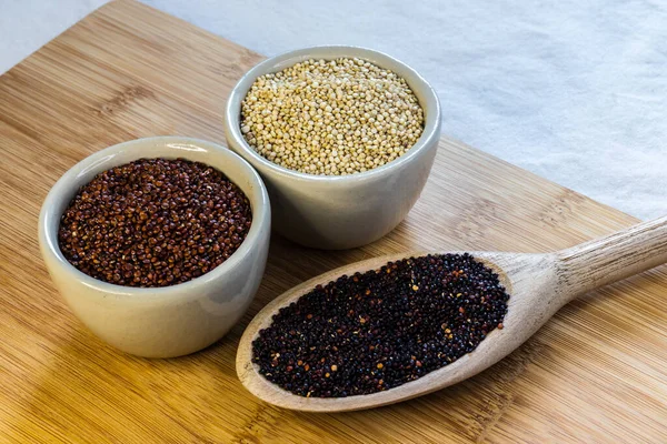 Ahşap arka planda kırmızı, siyah ve beyaz kinoa tohumları. Vejetaryen yemeği.