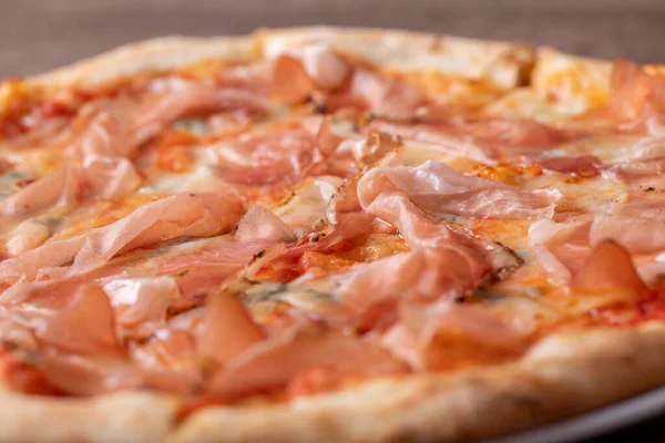 Ahşap bir masada jambon ve gorgonzola ile taze pişmiş pizzanın detayları.