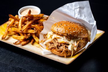 Siyah arka planda patates kızartması ve domuz etli lezzetli hamburgerin detayları.