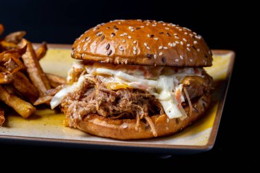 Siyah arka planda patates kızartması ve domuz etli lezzetli hamburgerin detayları.