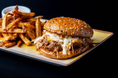 Siyah arka planda patates kızartması ve domuz etli lezzetli hamburgerin detayları.