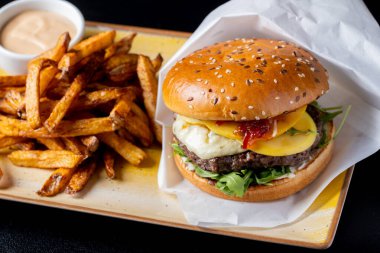 Gorgonzola peynirli lezzetli sığır burger ve siyah arka planda patates kızartması.