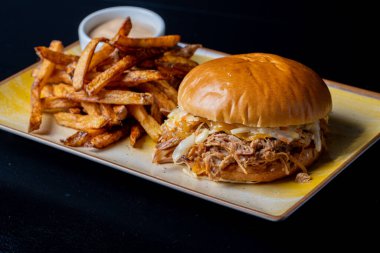 Siyah arka planda patates kızartması ve domuz etli lezzetli hamburgerin detayları.