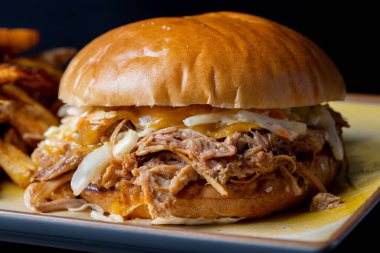 Siyah arka planda patates kızartması ve domuz etli lezzetli hamburgerin detayları.