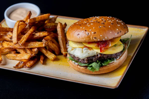 Gorgonzola peynirli lezzetli sığır burger ve siyah arka planda patates kızartması.