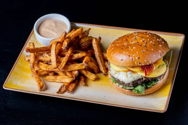 Gorgonzola peynirli lezzetli sığır burger ve siyah arka planda patates kızartması.