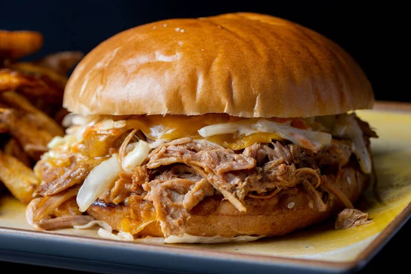 Siyah arka planda patates kızartması ve domuz etli lezzetli hamburgerin detayları.