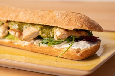 Ahşap masada yeşil soslu, taze ızgara hindi göğsü sandviçi.