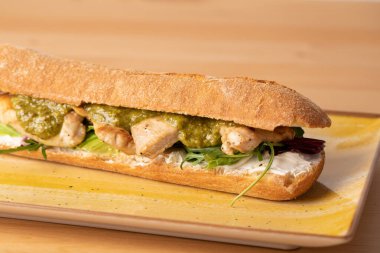 Ahşap masada yeşil soslu, taze ızgara hindi göğsü sandviçi.