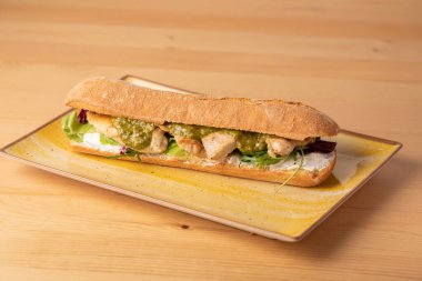 Ahşap masada yeşil soslu, taze ızgara hindi göğsü sandviçi.