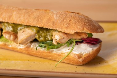 Ahşap masada yeşil soslu, taze ızgara hindi göğsü sandviçi.