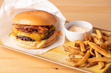 Tahta bir masanın üzerinde patates kızartması ve sosla sulu taze çizburgeri kapat.