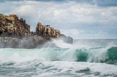 Kasvetli gökyüzü, keskin kayalar ve denizde büyük dalgalar olan deniz manzarası. Engebeli kayalıklar ve dönen deniz. Kayaların etrafında dönen beyaz suyla engebeli, kayalık kıyı şeridi.