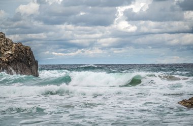 Sahilde Gökyüzüne Karşı Kaya oluşumları. Kıyısında ve sularında büyük kayalar olan güzel bir okyanus sahili. Okyanustaki güçlü dalgalar. Okyanus suyu, kayalık sahillerde, engebeli kayalıklarla sıçrıyor.