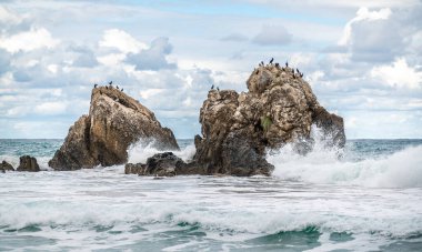 Okyanus suyu, güzel gökyüzü ve bulutlarla kayalık sahillere sıçrar. Kışın deniz kıyısında taşa vuran deniz dalgaları. Kayaların etrafında dönen beyaz suyla kayalık kıyı şeridi