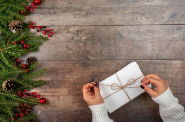 Noel hediyesi kutusu. Dişiler Noel hediyesini açar, güzel manzara, Aralık tatili hazırlıkları, bayram gelenekleri, firavun ağacı brunch 'ı, ahşap arka planda çam kozalağı