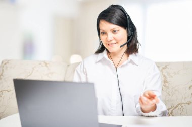 İş videosu konferansı. İş kadını bilgisayarını kullanarak iş arkadaşlarıyla konuşuyor. Evdeki oturma odasından akıllı çalışmalarını söylüyor. Kadın girişimci, dizüstü bilgisayarda müşteri video konferansı öneriyor