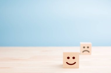 Güler yüzlü ahşap küpler ve ahşap masada hüzünlü bir tane, mavi arka plan. Mesaj için yer var. duygusal durum kavramı